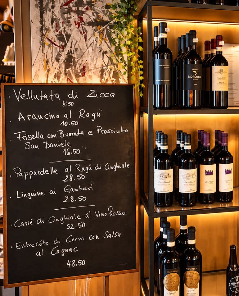 Die Saisontafel im Restaurant mit den Gerichten der Saison, daneben das beleuchtete Weinregal